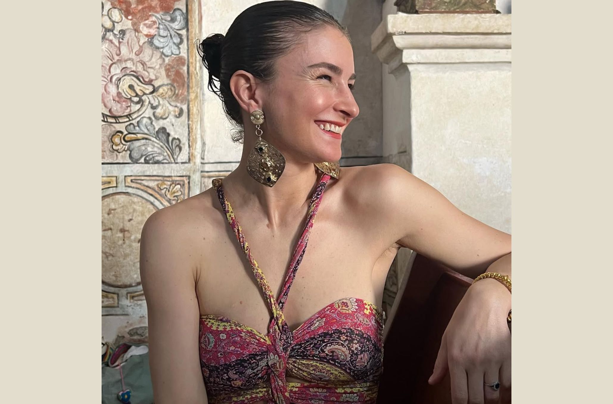 Γυναίκα με μεγάλο σκουλαρίκι και πιασμένα μαλλιά κοιτάζει χαμογελαστή