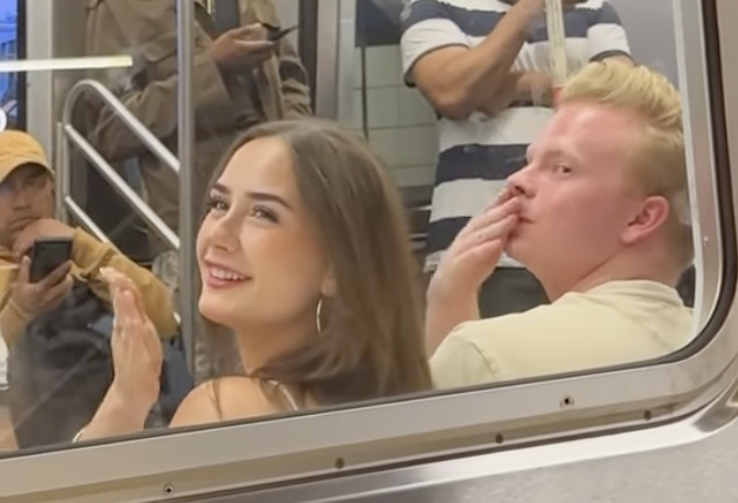 Γυναίκα χαμογελαστή και δίπλα της ξανθός άντρας που στέλνει φιλί με το χέρι του στο στόμα