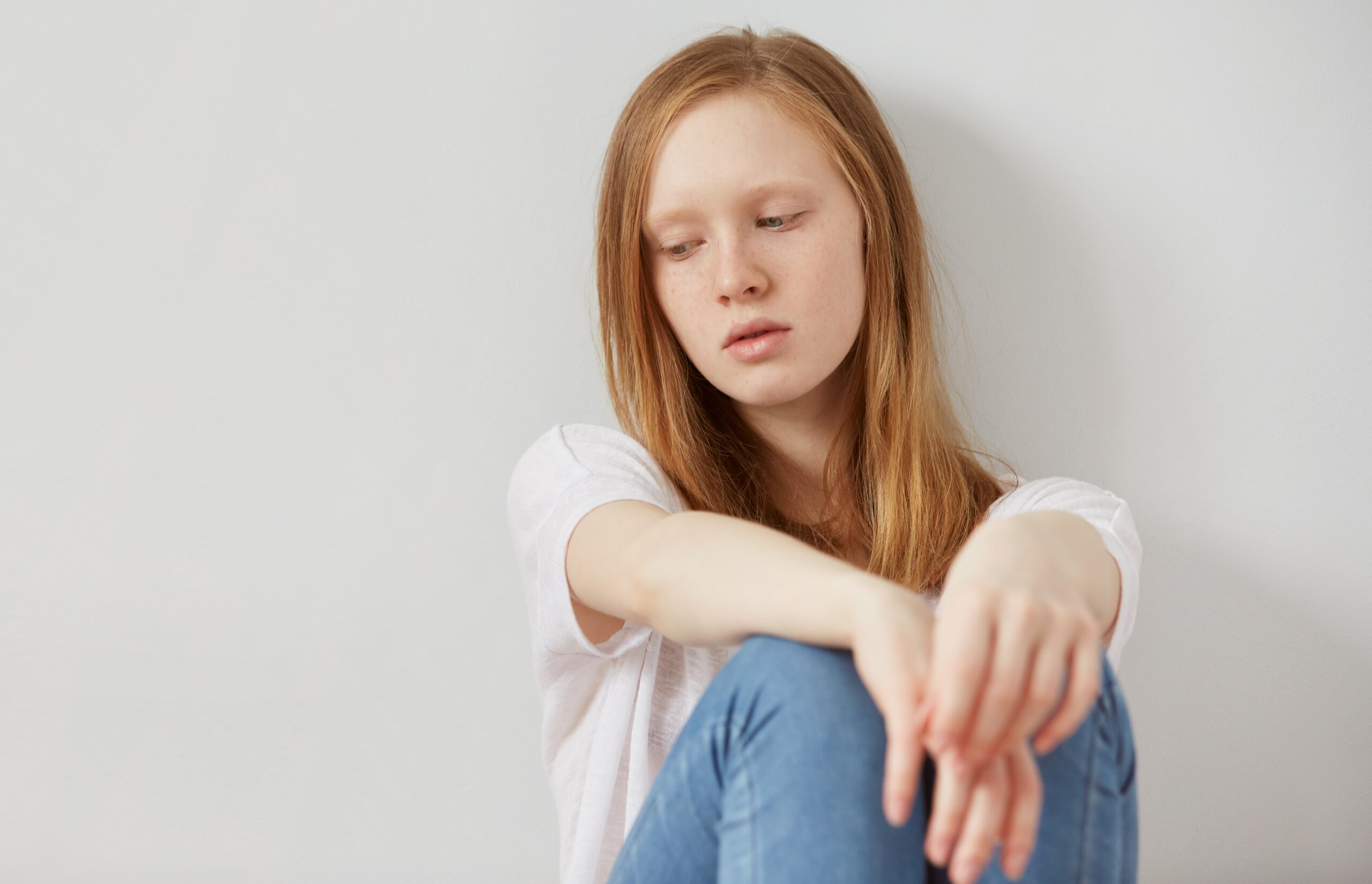 Κορίτσι με ξανθά μαλλιά και τζιν παντελόνι κάθεται στεναχωρημένη