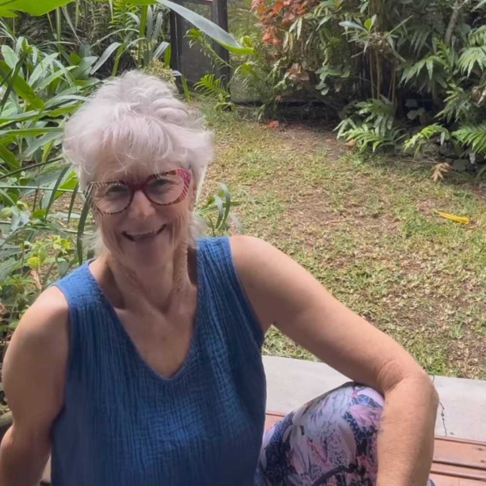 Γυναίκα με κοντά λευκά μαλλιά χαμογελαστή κάθεται σε κήπο