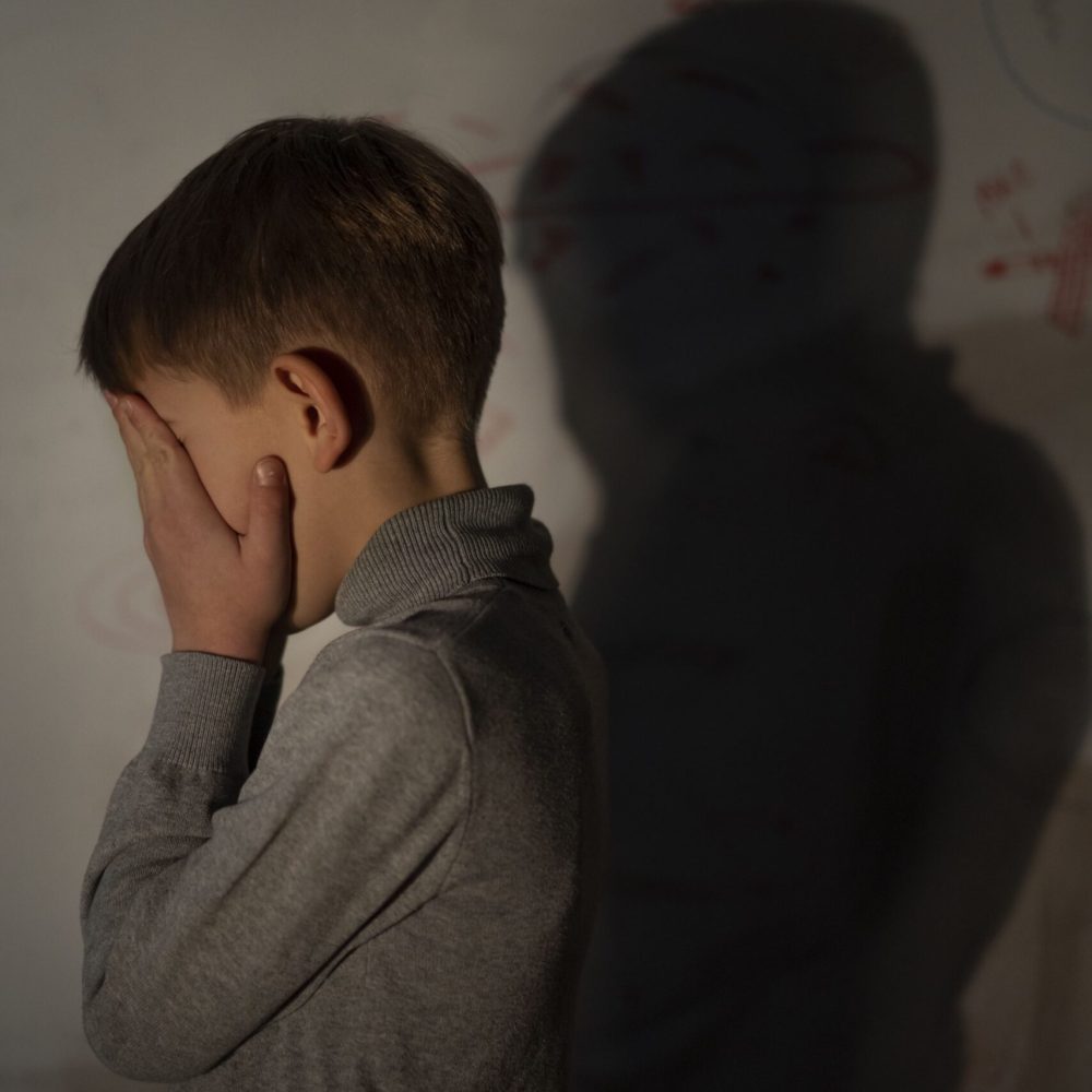 Αγόρι στεναχωρημένο με τα χέρια στο πρόσωπο και σκιά στον τοίχο