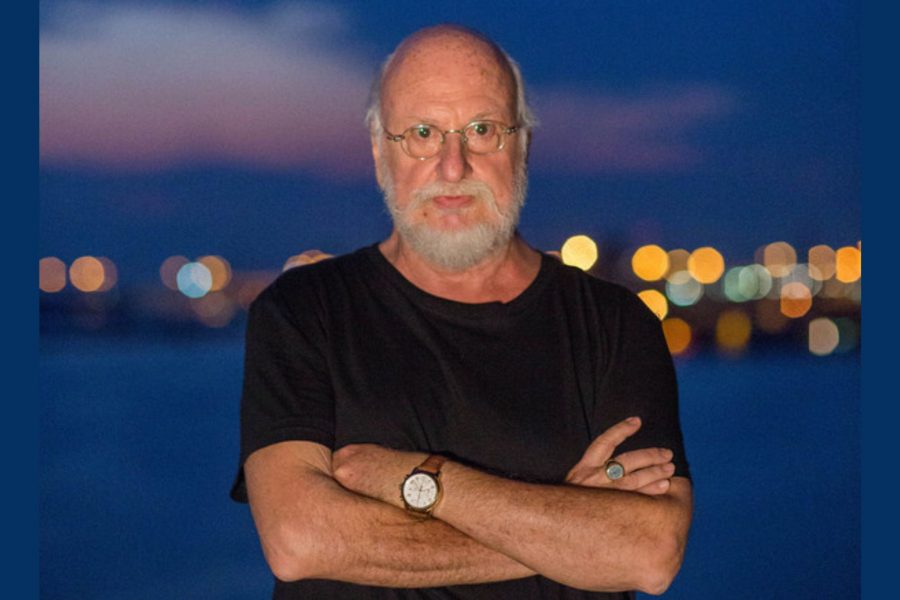 Άντρας με λευκά γένια και σταυρωμένα χέρια, φοράει μαύρο κοντομάνικο μπλουζάκι, γυαλιά μυωπίας και ρολόι στο χέρι