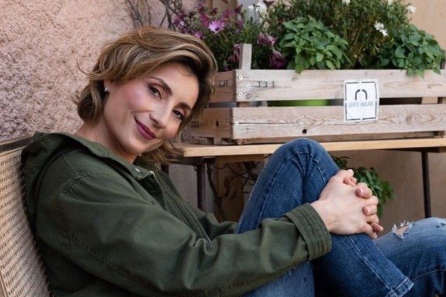 Γυναίκα με λαδί ζακέτα και τζιν παντελόνι κάθεται και κρατάει το πόδι της με τα χέρια της