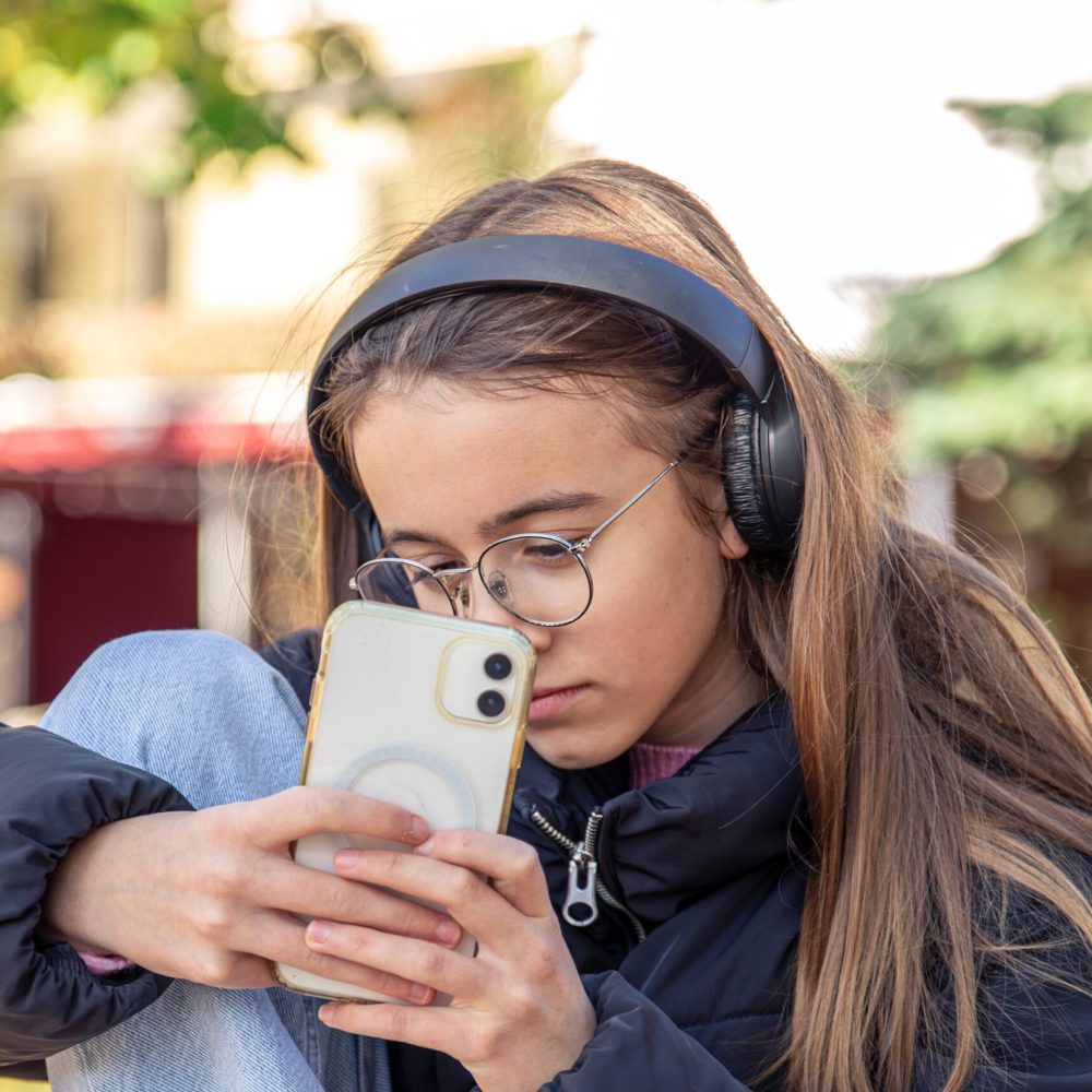 A cute teenage girl is taking pictures on the phone. Girl in headphones. High quality photo. A girl in headphones takes a photo with a phone.