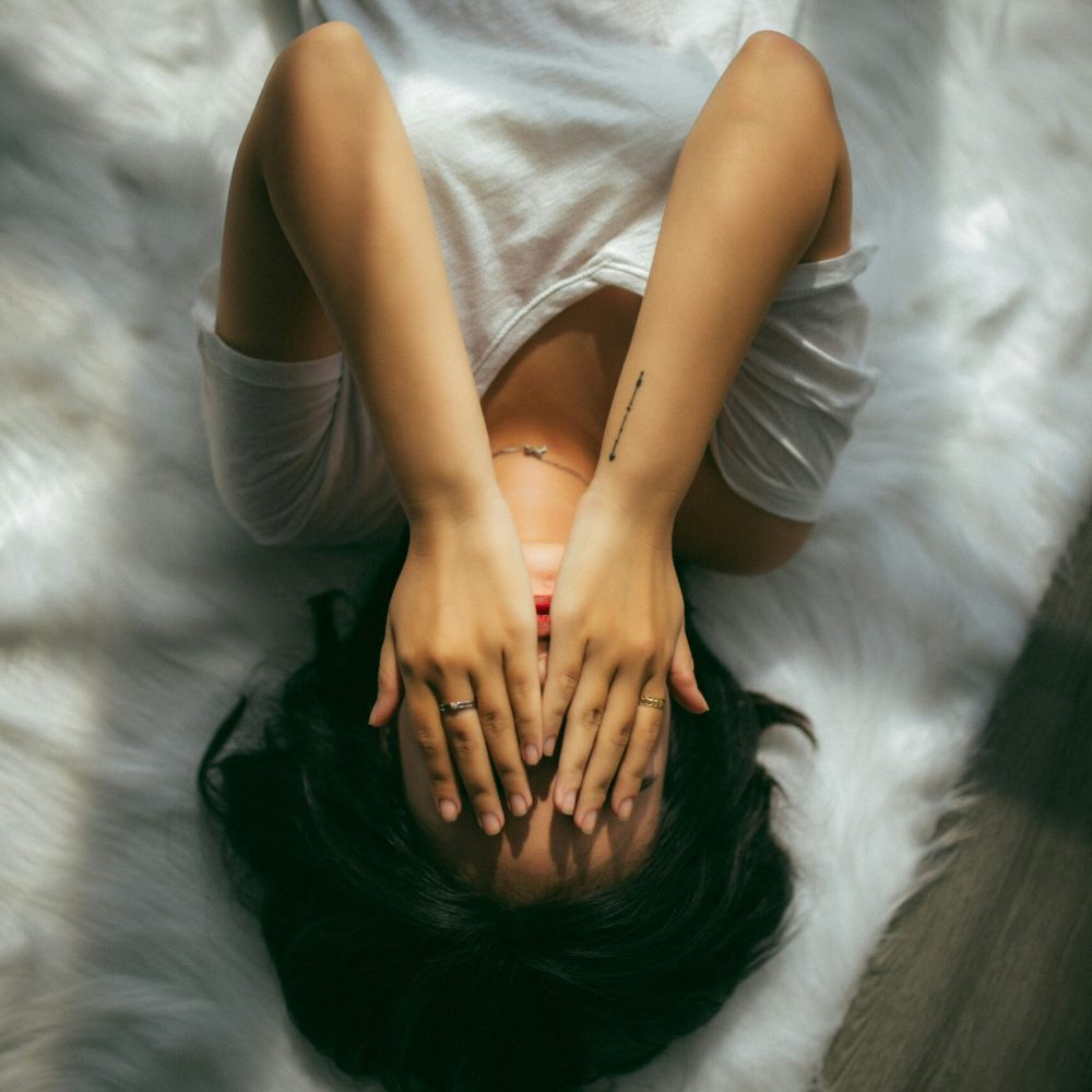 γυναίκα κρύβει με τα χέρια της το πρόσωπο και είναι ξαπλωμένη στο κρεβάτι