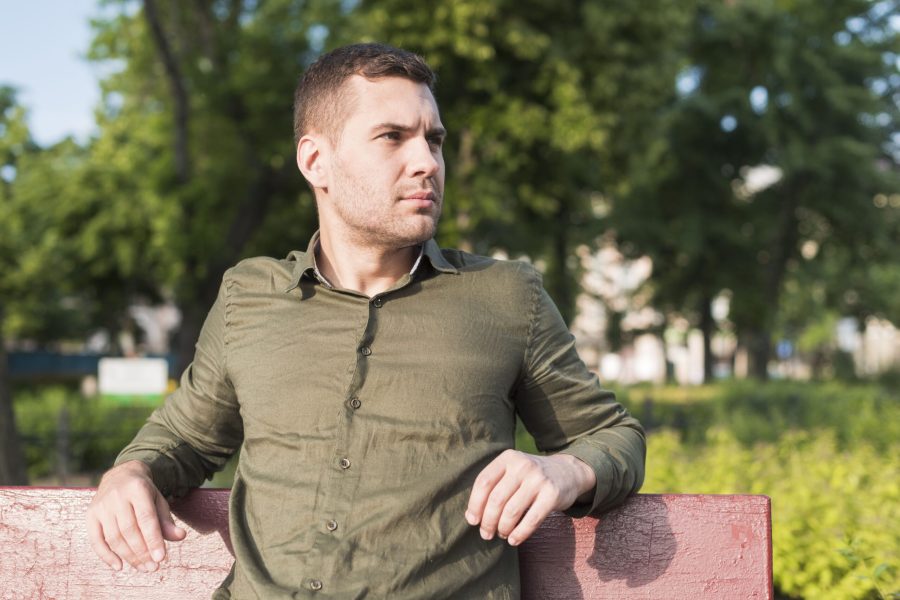 Άντρας με λαδί πουκάμισο κάθεται σε παγκάκι