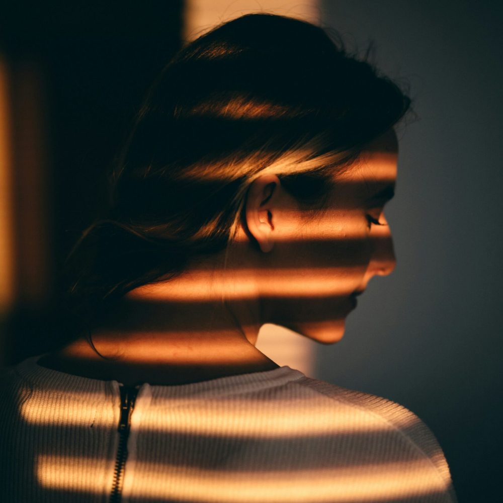 woman-standing-in-front-of-a-window-with-the-sun-shining-through-the-blinds-unsplash