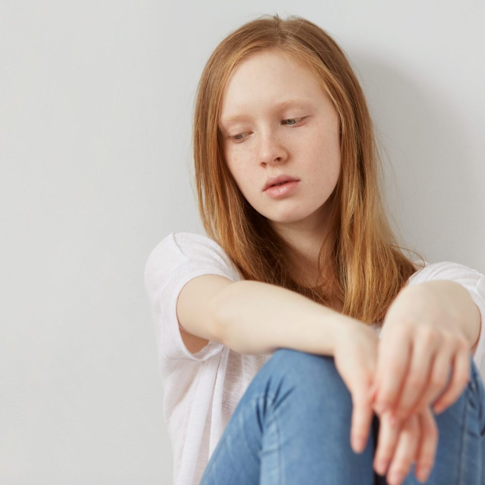 Κορίτσι με ξανθά μαλλιά και τζιν παντελόνι κάθεται στεναχωρημένη